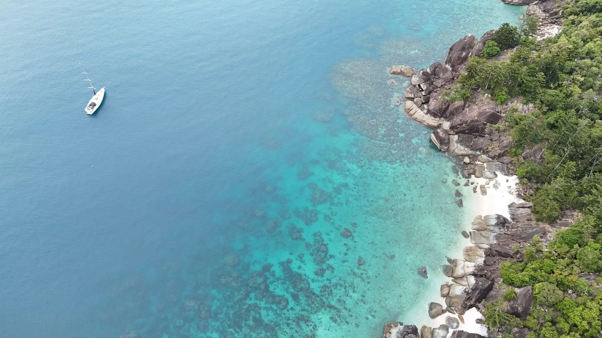 Shimbiri anchored alone off a turquoise reef-fringed shore